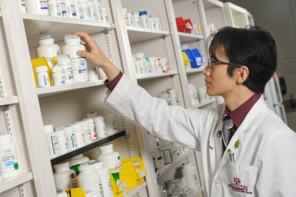 Pharmacy Student Reaching For Bottle Of Pills.