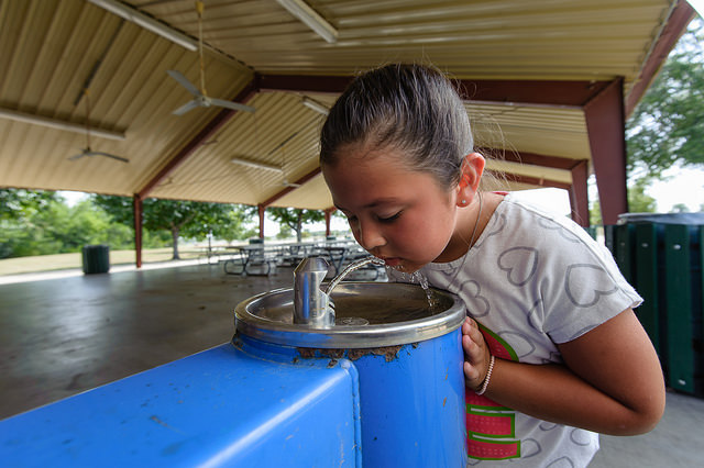 Young girl drinking from a water fountain.