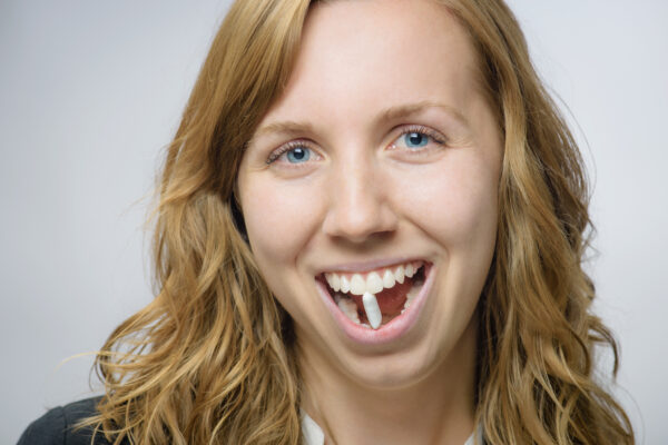 Woman Smiling Playfully Holding A Piece Of Gum Between Her Teeth.