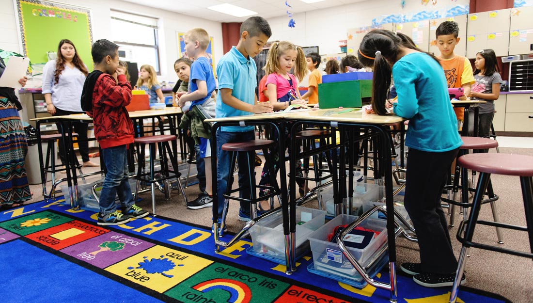 Young children in a classroom using standing desks.