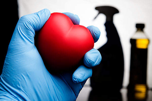 Gloved Hand Holding Up Toy Heart, Background Shows Chemicals.