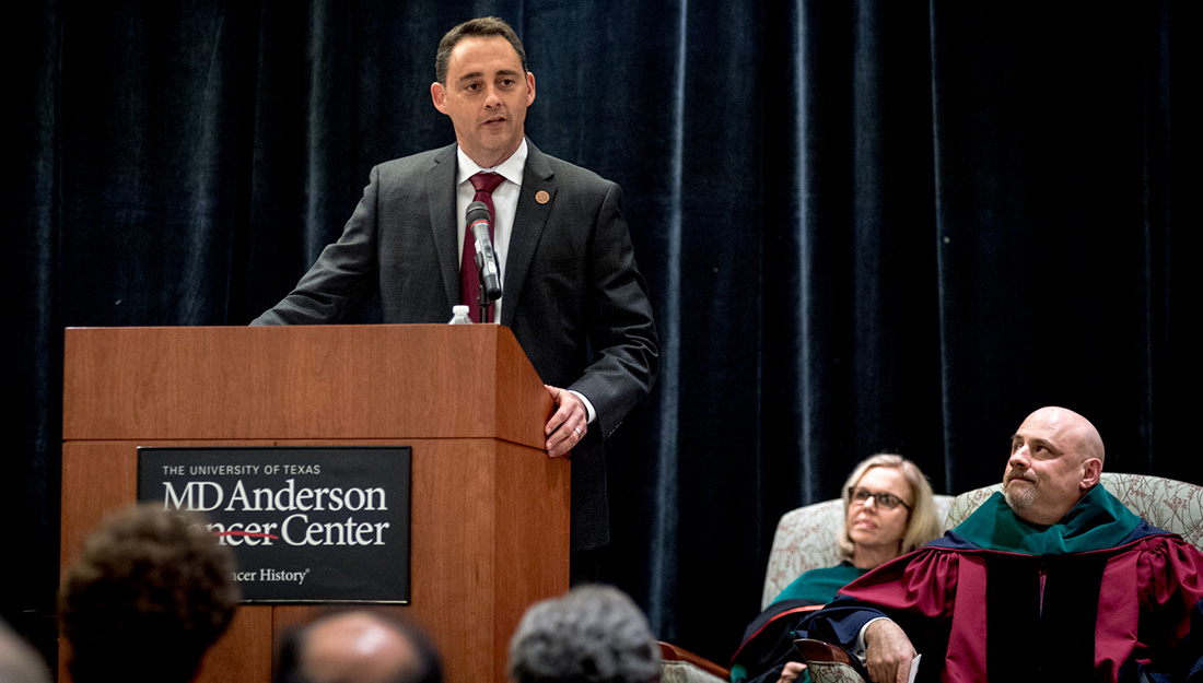 Medical student Rhett Butler speaks to the crowd with onlookers sitting on stage listening