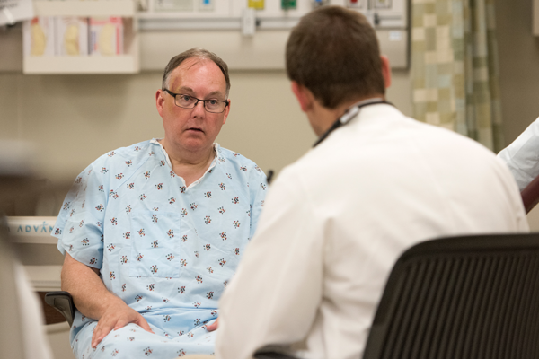 Man In A Hospital Gown Speaking With A Physician In A White Coat About His Pain Levels