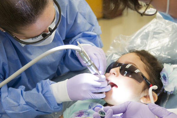 Give Kids A Smile - A Dentistry Professional Performs A Dental Procedure On A Child.