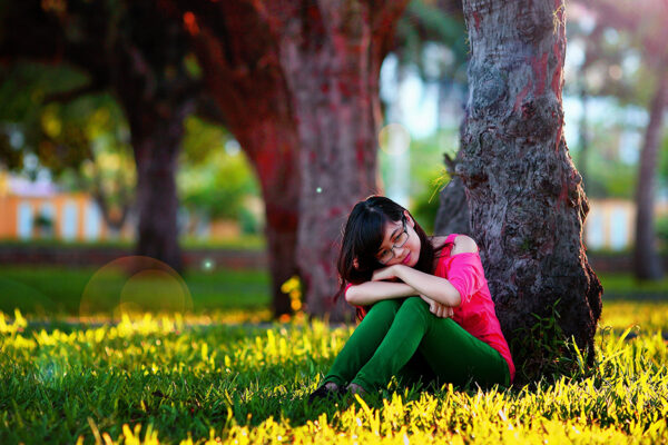 Mental Health - A Girl Sitting In The Grass Under A Tree With Her Head Resting On Her Knees