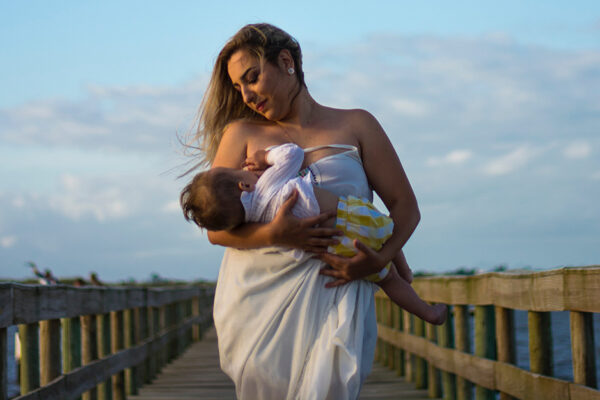 Breastfeeding_mastitis_blocked Milk Ducts_a Woman Holds Her Breastfeeding Baby On A Pier By The Water