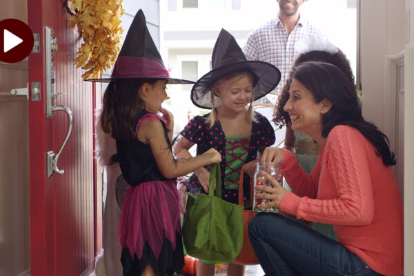 A Woman Is Giving Candy To Two Children Dressed As Witches