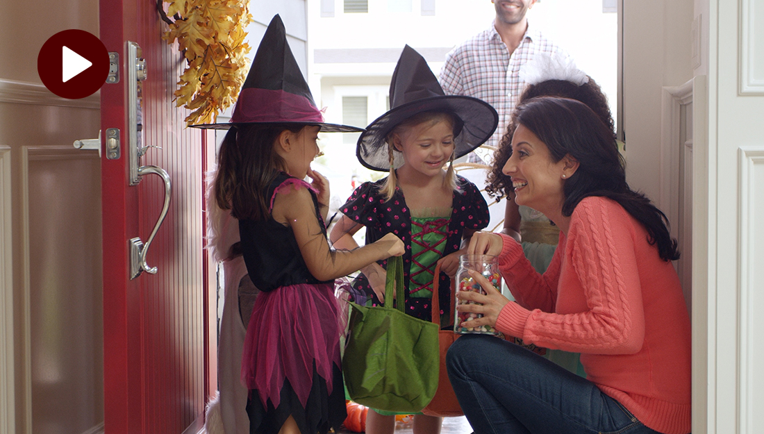 A woman is giving candy to two children dressed as witches