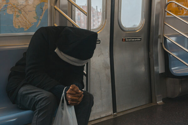 A Man Sitting On A Bus Hunched Over To Represent Chronic Pain