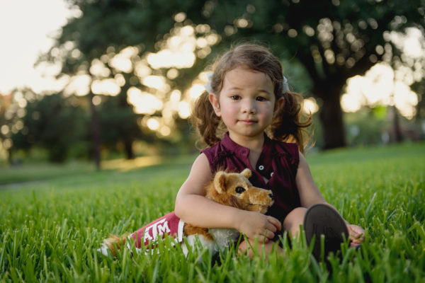 Childhood Development_Child Development_A Young Girl Is Sitting In Grass Holding A Stuffed Animal