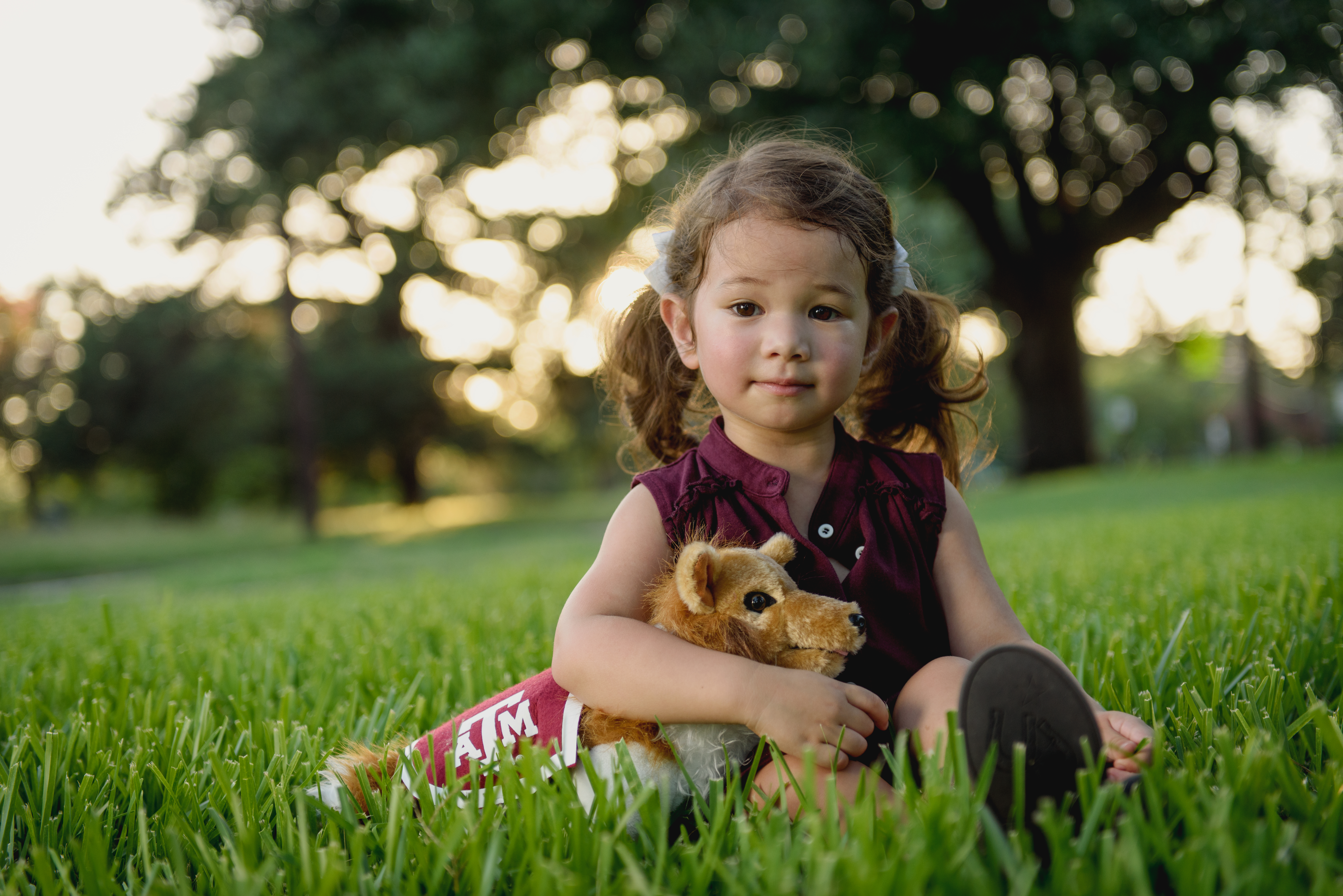 Childhood development_Child development_A young girl is sitting in grass holding a stuffed animal