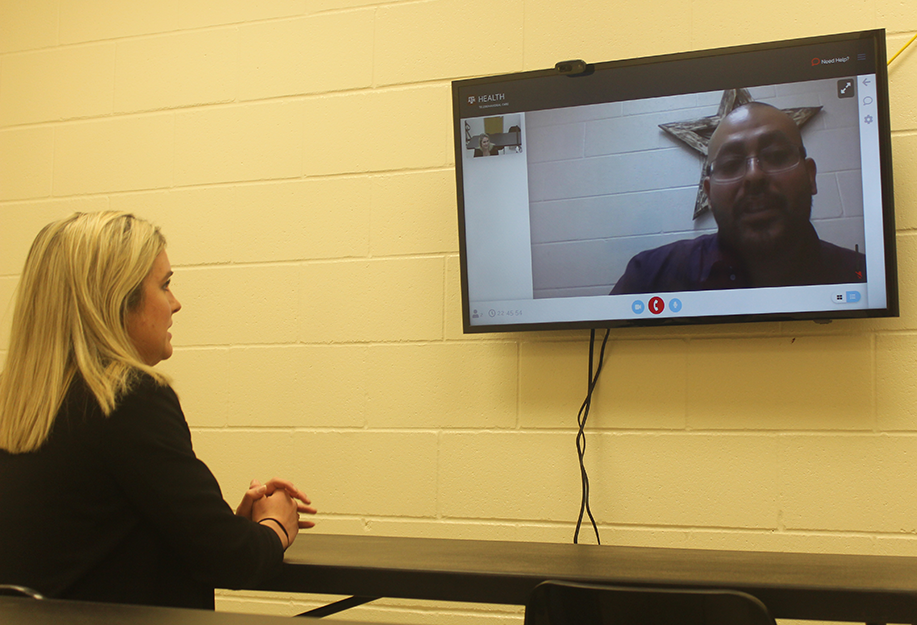 Washington County Jail_A woman sits at a table and speaks to a man on a television