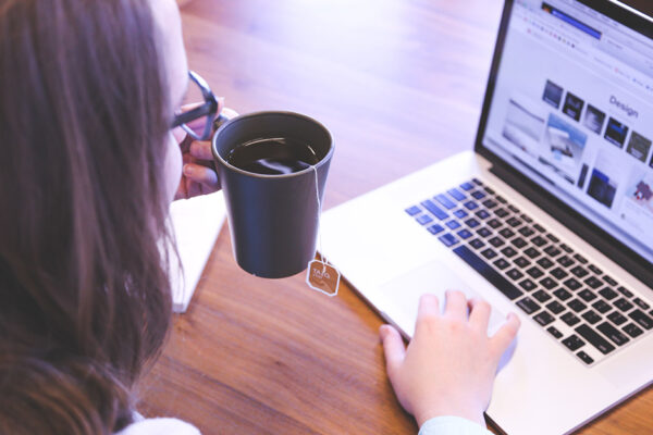 Woman Drinking Tea And Using Laptop In Home Workspace