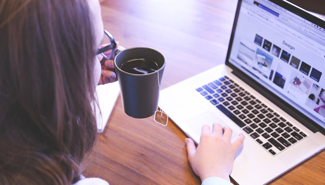 woman drinking tea and using laptop in home workspace