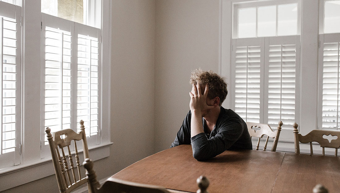 man resting head in hand sitting at table