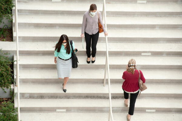 Three Women Walk On Staircase, Each Wearing A Surgical Mask.