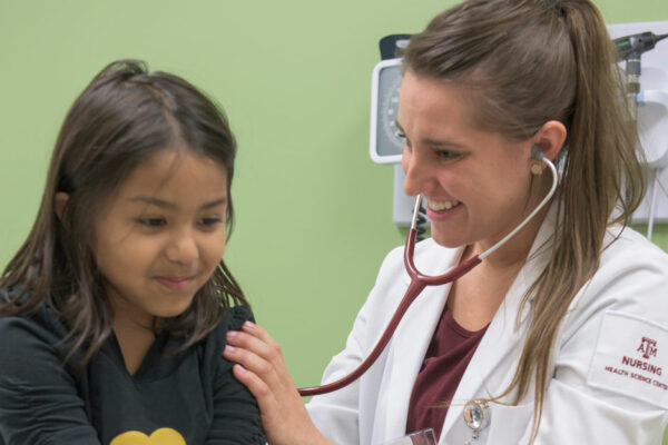 Female Family Nurse Practitioner Student Uses Stethoscope To Check Heart And Lung Sounds On Hispanic Pediatric Patient