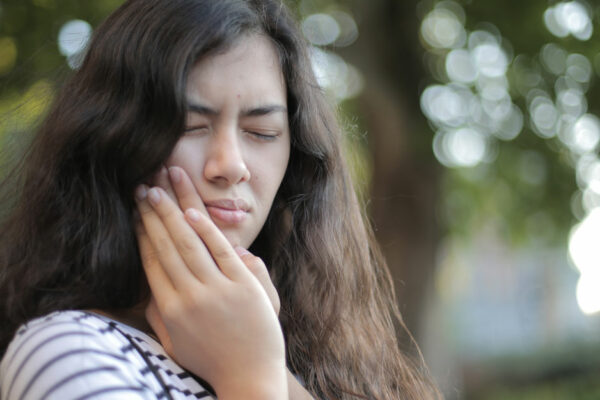 A Woman With Long Brown Hair Clenches Her Jaw With Eyes Closed As If In Pain