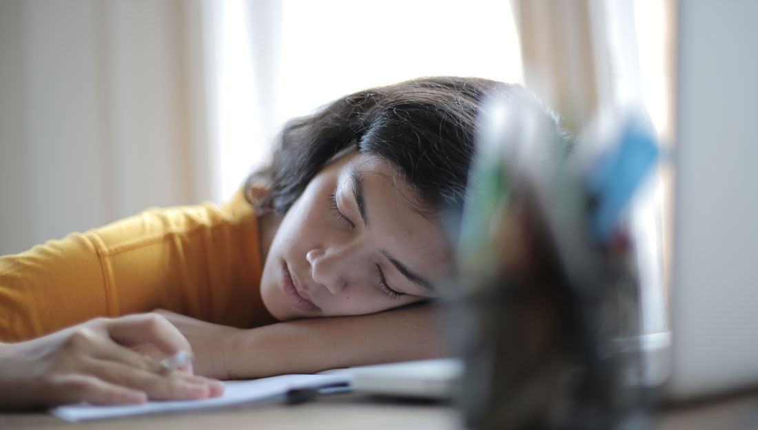 woman in yellow shirt sleeps at desk with her head resting on her arms