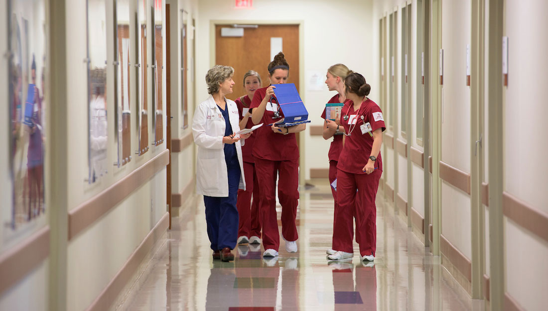 photo of nursing students in scrubs walking down a hallway with a professor in a white coat