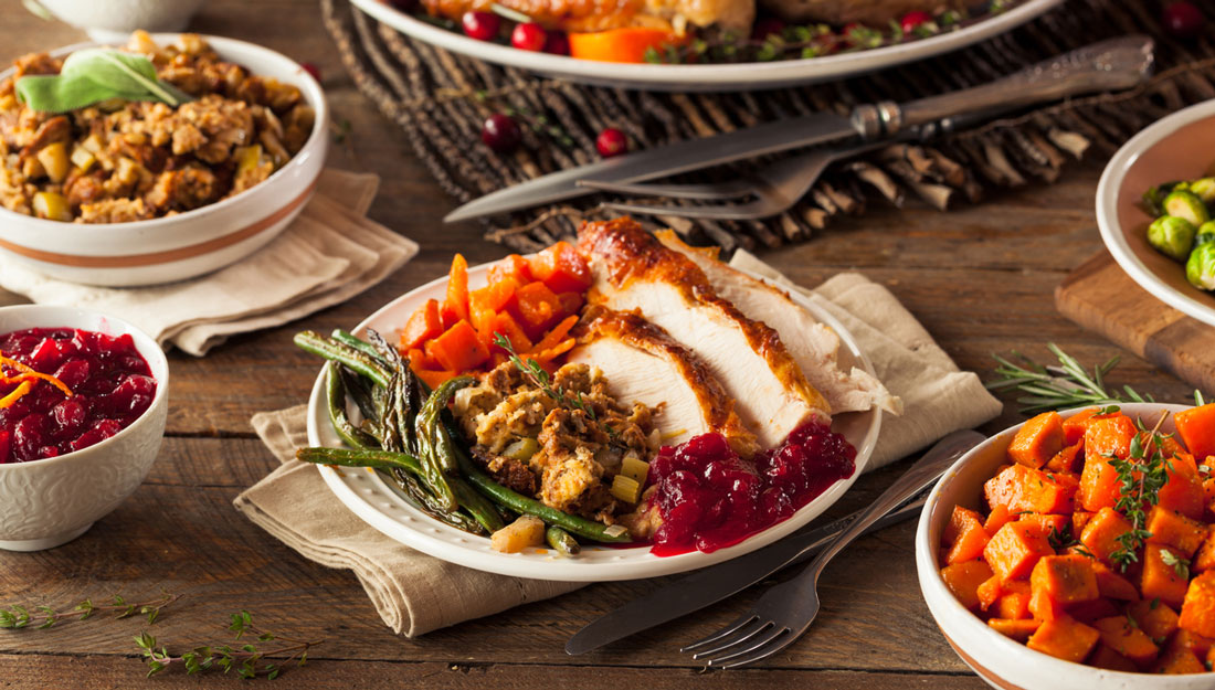 table full of Thanksgiving food, plate of turkey, stuffing, sweet potatoes, asparagus and cranberry sauce