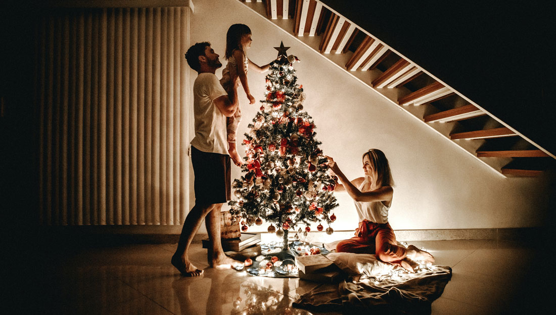 family of three decorates a Christmas tree in their home