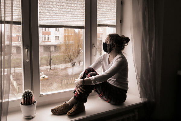 А Young Woman In A Protective Mask Sits On The Window Sill. Du