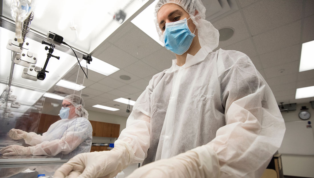 two people wearing personal protective equipment work in a laboratory