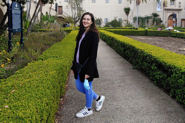 Lacy Failla Stands On A Hedge-lined Sidewalk In A Park