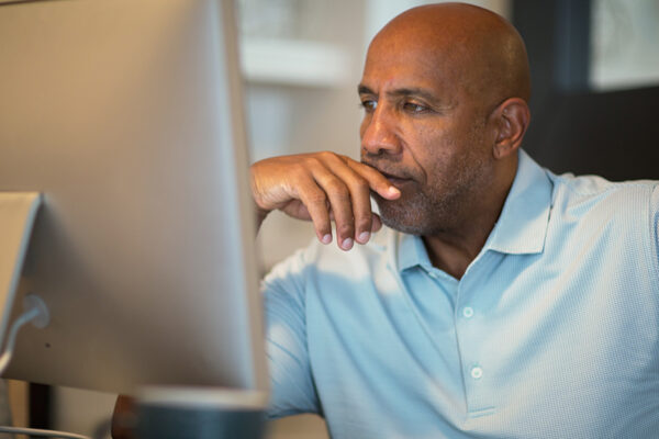 African American Man Holding Hands In Front Of Face While Looking At Computer.