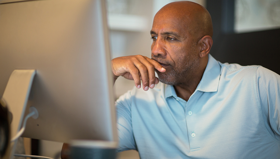 African American man holding hands in front of face while looking at computer.