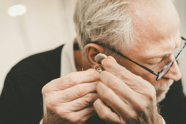 Older Man Places Hearing Aid In His Ear