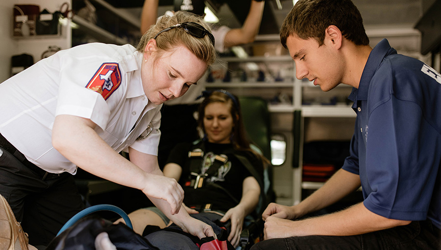 two emergency medical responders work together on a patient in the back of an ambulance