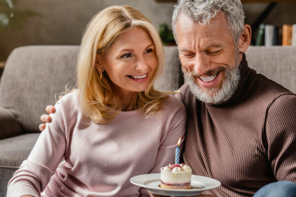 Middle Aged Man Sits With Woman On Couch While Holding A Cupcake With A Candle