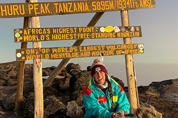 Peyton Sits Below The Mount Kilimanjaro Highest Point Wooden Sign.