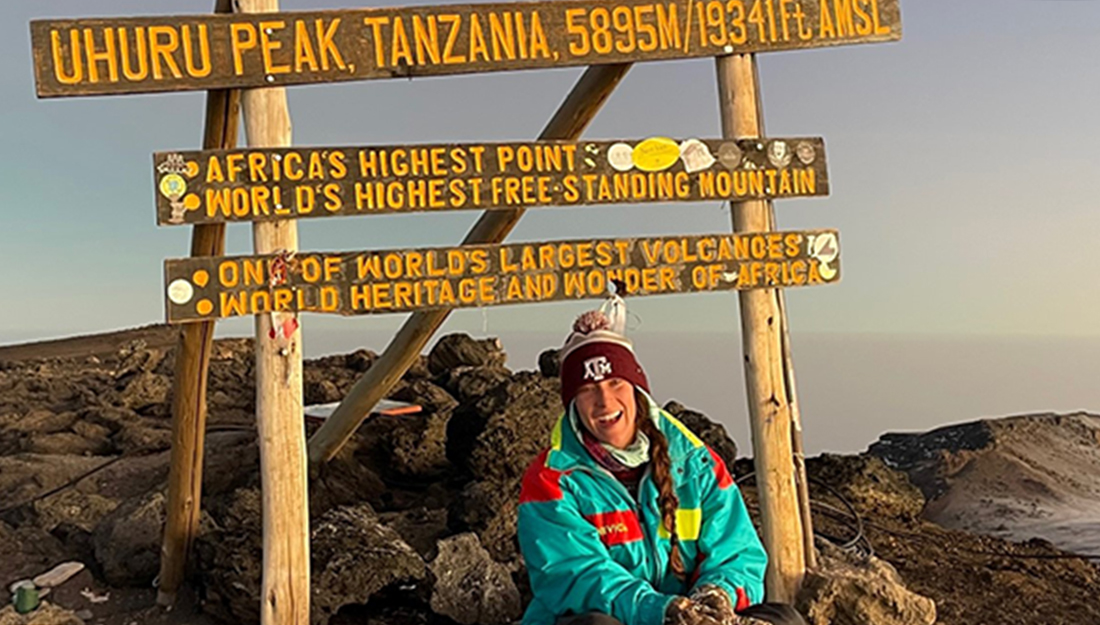 Peyton sits below the Mount Kilimanjaro highest point wooden sign.