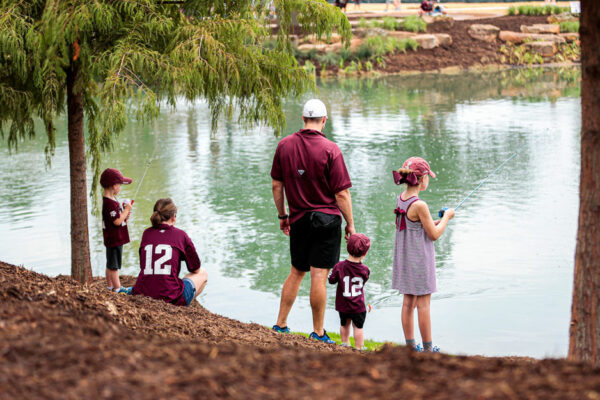 Parents And Their Three Young Children Dressed In Texas A&M Fan Gear Spend Time In Nature At Aggie Park