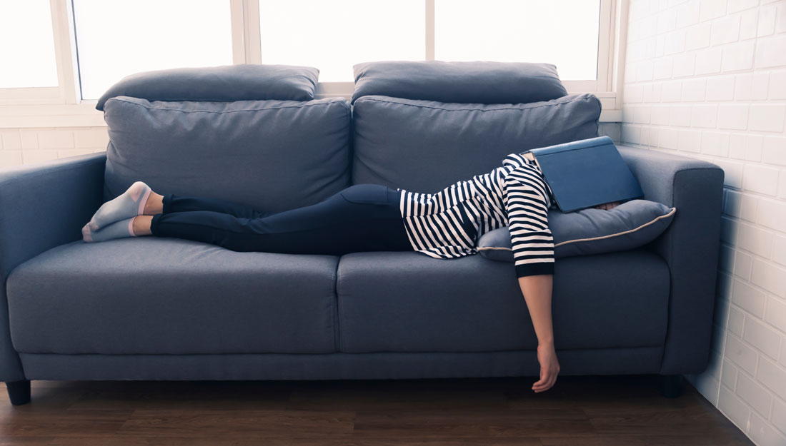 woman naps on a couch with her head under a book