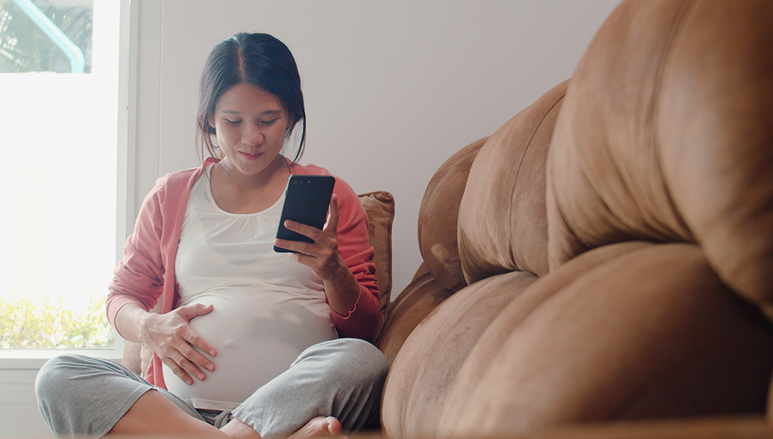 Young pregnant woman using mobile phone on a couch.