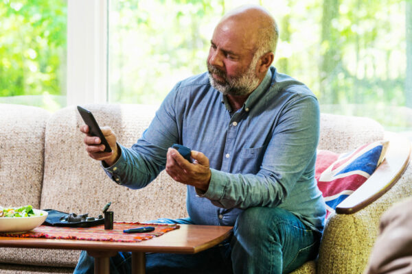 Mature Diabetic Man Testing His Blood Sugar And Using A Smartphone