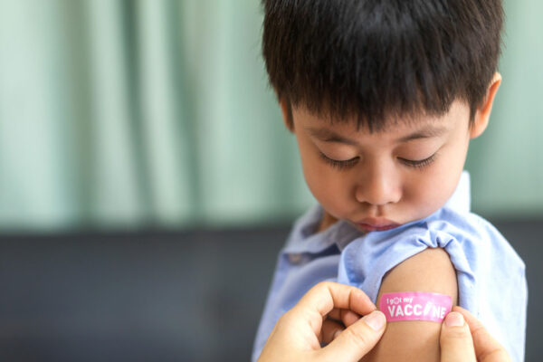 Boy Looks Down At Bandaid Being Placed On His Arm After Receiving A Vaccination