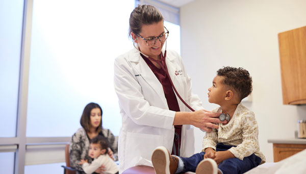 physician checks pediatric patient's heart sounds in a clinic exam room