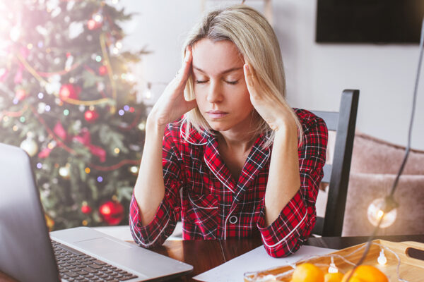 Worried Sad Middle Aged Woman Working At The Home Office During Christmas Holiday. Stressed Upset Female Looking At Screen Of Laptop By Christmas Tree