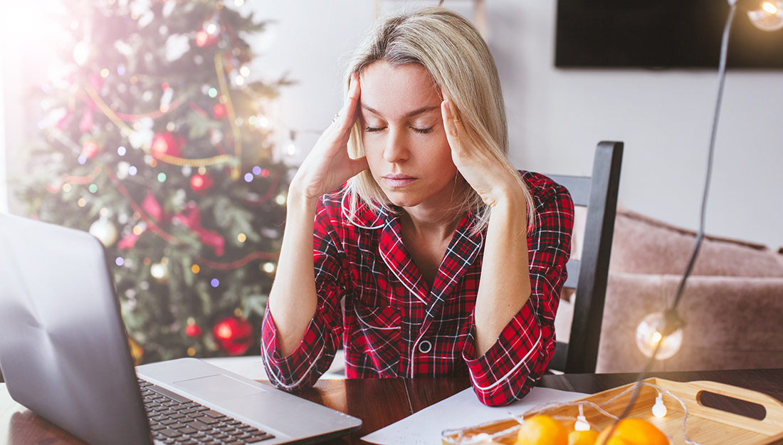 Worried sad middle aged woman working at the home office during Christmas holiday. Stressed upset female looking at screen of laptop by Christmas tree