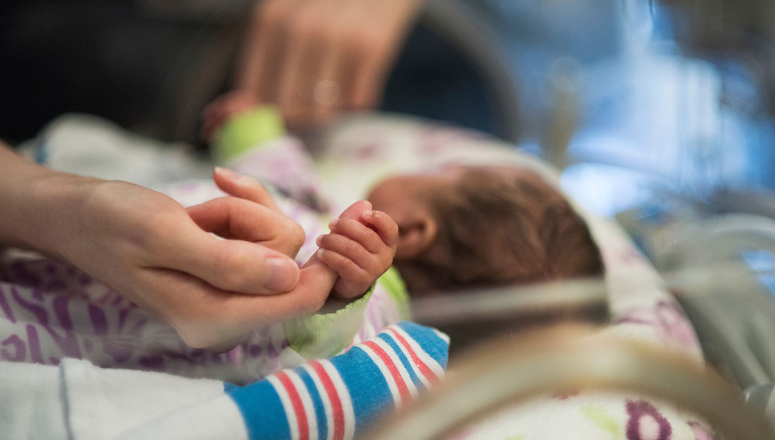 tiny baby hand holds an adult woman's finger