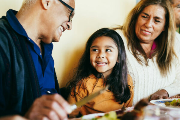 Happy Hispanic Grandparents Eating With Granddaughter At Home Patio