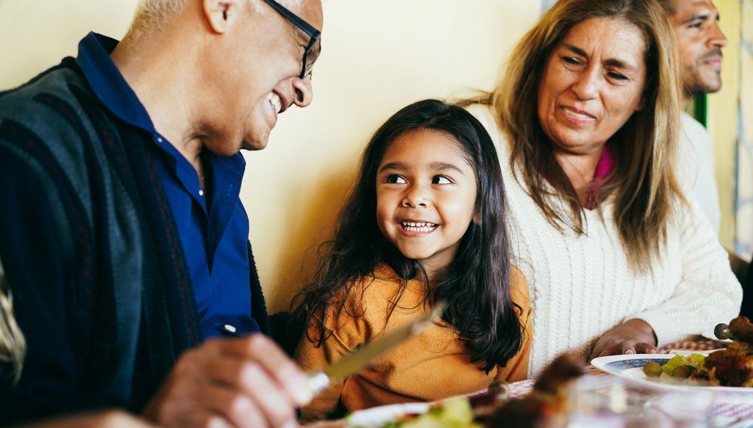 Happy Hispanic grandparents eating with granddaughter at home patio