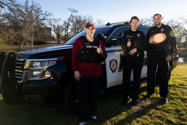 Three People In Uniform Pose For A Portrait In Front Of A University Police Department Vehicle