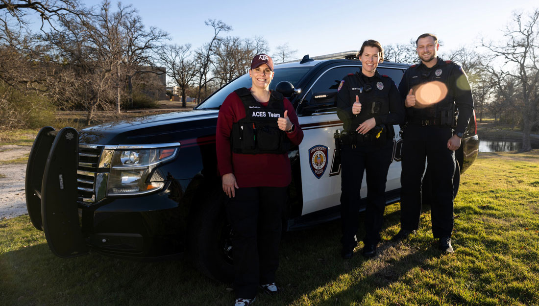 three people in uniform pose for a portrait in front of a University Police Department vehicle