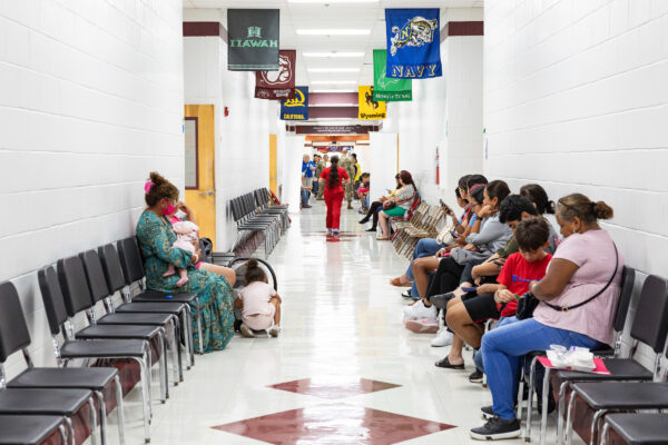 people sit in chairs lined up along a high school hallway